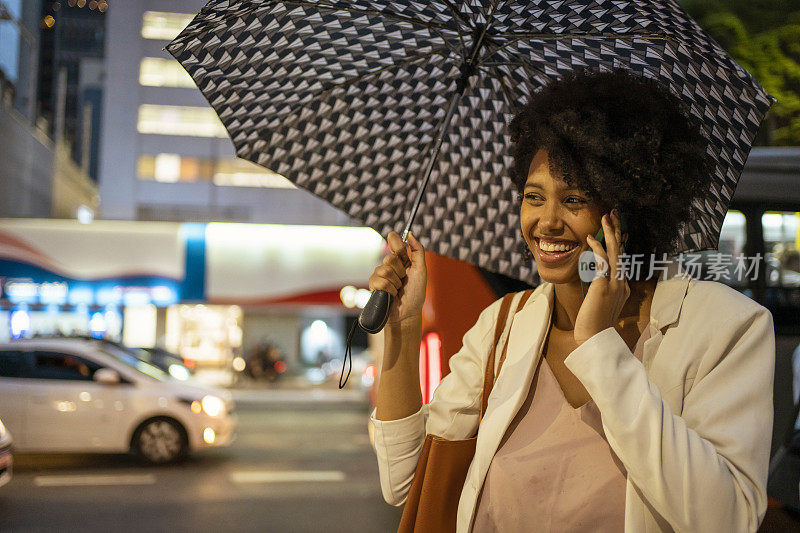 在圣保罗大道(Avenida Paulista)，一名女子打着雨伞用智能手机聊天，São Paulo，巴西。